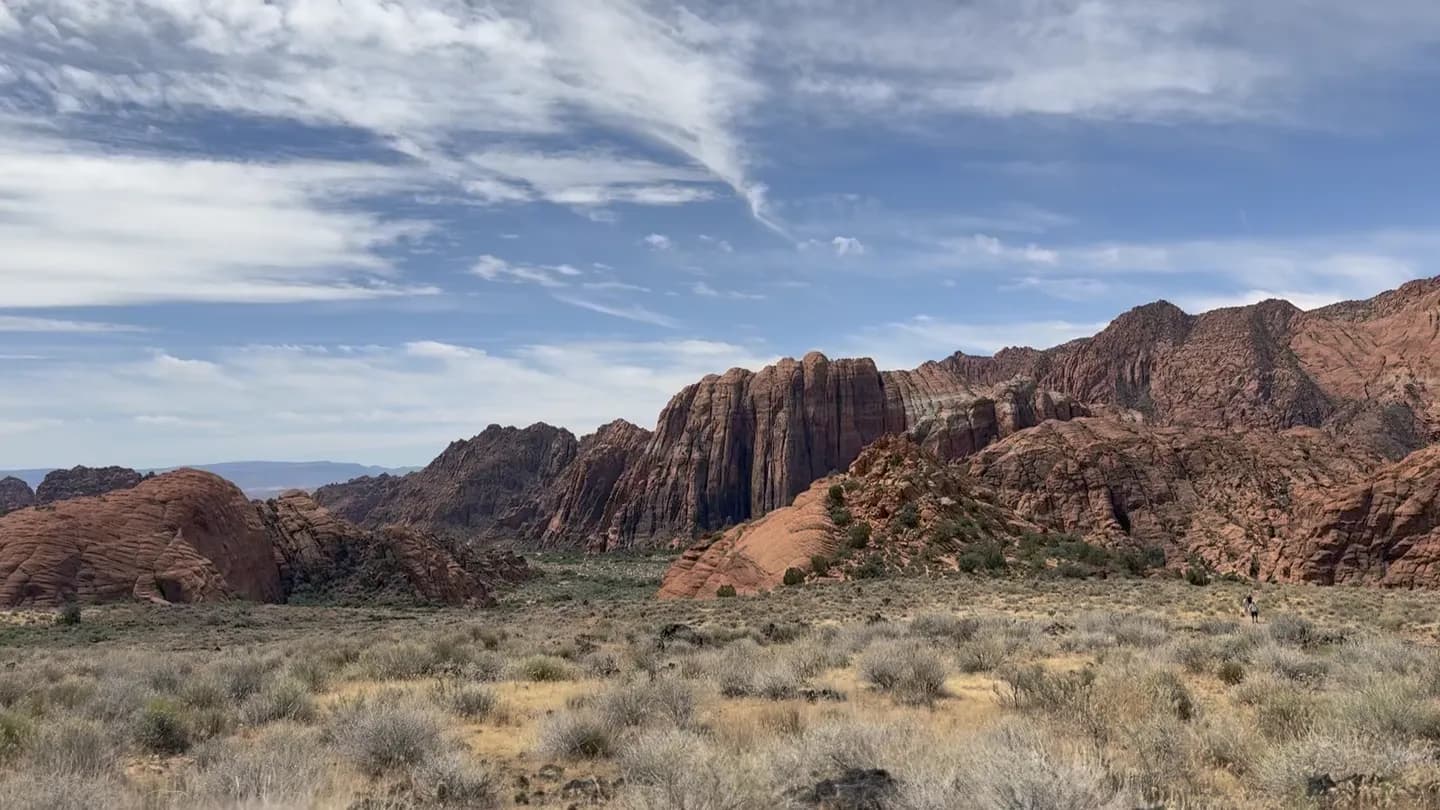 A hiker on a desert trail beneath red rock spires near St. George, Utah